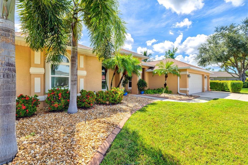 A tan stucco house features a concrete walkway, palm trees, and a gravel landscaping bed — 203 LAKE VICTORIA COURT, ENGLEWOOD, FL