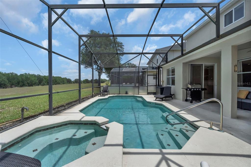 A screened-in pool and hot tub area overlooks a large grassy field — 711 KETTERING ROAD, DAVENPORT, FL