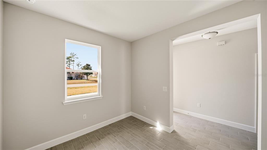 A room with light gray walls, wood-look tile flooring, and a window overlooking a neighborhood — 34 SEVILLE ORANGE PATH, PALM COAST, FL