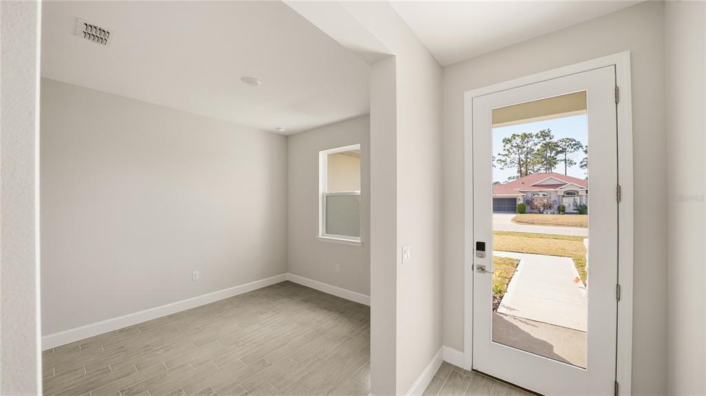 An interior view shows a room with gray tile flooring and a glass-paneled front door — 34 SEVILLE ORANGE PATH, PALM COAST, FL