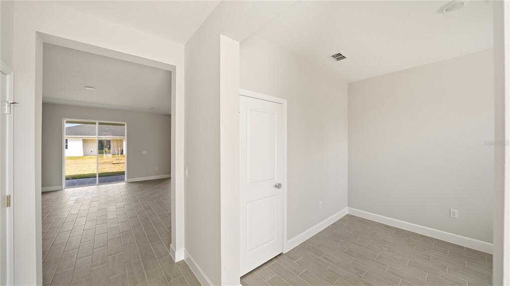 A room with light gray walls and tile flooring leads to an open living area — 34 SEVILLE ORANGE PATH, PALM COAST, FL