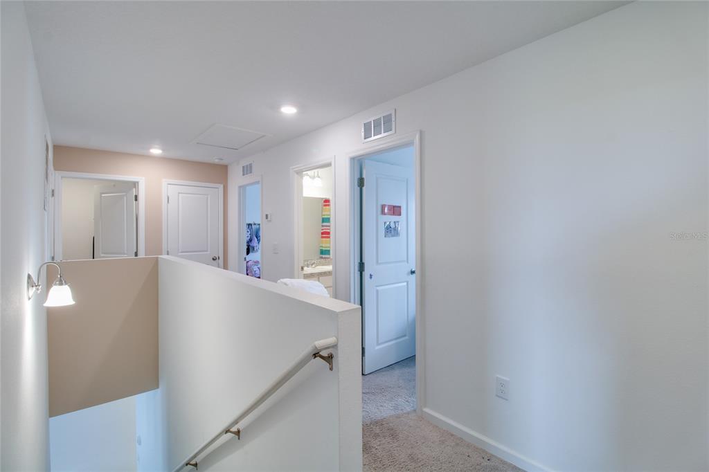 A carpeted hallway features a staircase railing, multiple white doors, and neutral wall paint — 8732 SPORTSMAN LOOP, GROVELAND, FL
