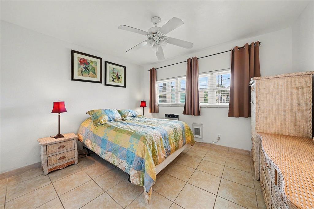 A sunroom features tile floors, a sofa, a desk, and large windows overlooking a parking lot — 7050 SUNSET WAY UNIT 11, ST PETE BEACH, FL