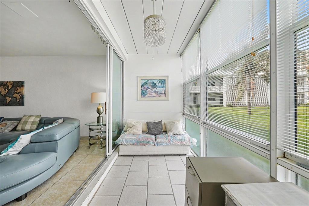 A bedroom features a bed with a colorful quilt, wicker furniture, and tile flooring — 7050 SUNSET WAY UNIT 11, ST PETE BEACH, FL