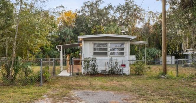 A single-story mobile home with a metal roof sits behind a chain-link fence — 9300 KIOWA DR, NEW PORT RICHEY, FL