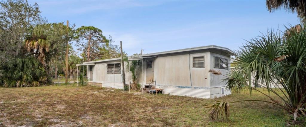 A single-story mobile home with metal siding sits on a grassy lot with palm trees — 9300 KIOWA DR, NEW PORT RICHEY, FL