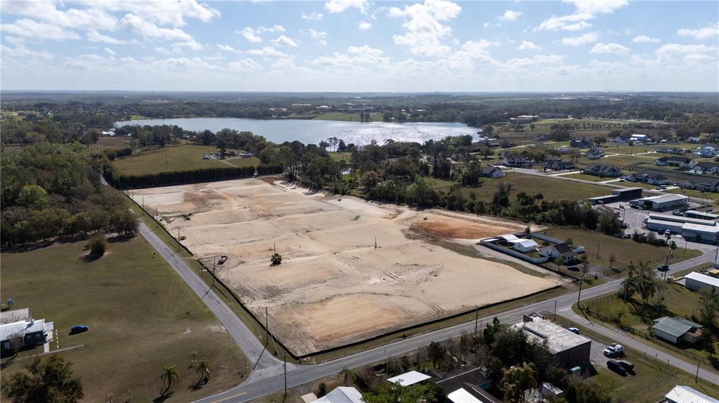 An aerial view shows a cleared, rectangular construction site bordered by roads and a lake — 32760 DUNNE ROAD, SAN ANTONIO, FL