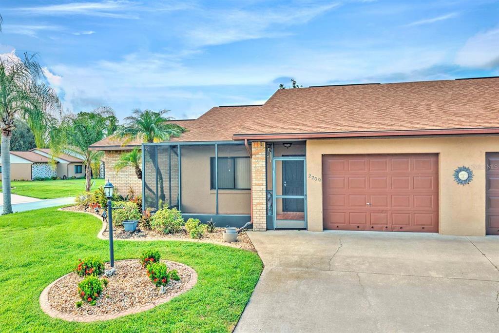 A single-story house with a brown shingled roof, a garage, and a screened-in front porch — 2209 HIDDEN CREEK CIRCLE, SEBRING, FL