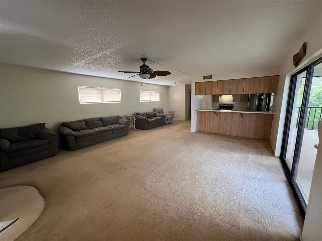 A living room with beige carpet, a ceiling fan, and an open kitchen with wood cabinets — 4403 7TH STREET E UNIT 7, ELLENTON, FL