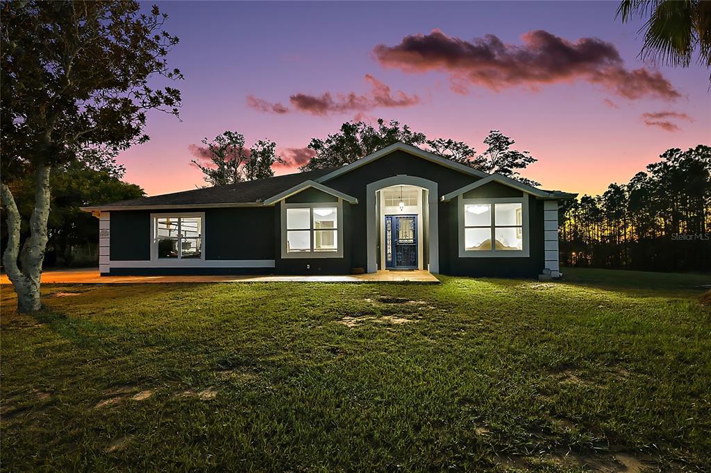 A dark-painted single-story house with a front porch and illuminated windows at sunset — 14520 LOST LAKE ROAD, CLERMONT, FL