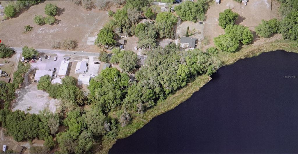 An aerial view shows a residential property with multiple buildings, trees, and a large lake — 0 KNIGHT STREET, MASCOTTE, FL