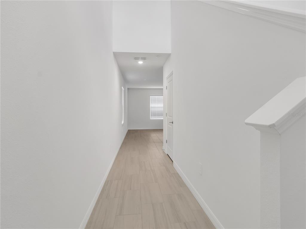 A bright hallway features light wood-look tile flooring, white walls, and a staircase railing — 8505 BELLA MAR TRAIL, PARRISH, FL