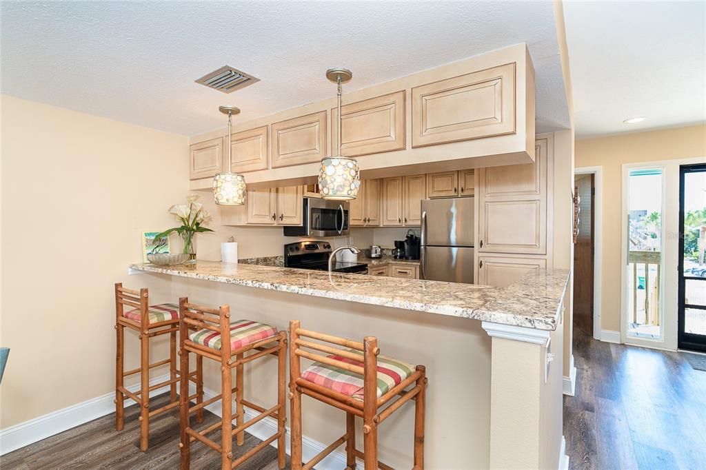A kitchen features light wood cabinets, granite countertops, a breakfast bar, and three bamboo stools — 301 S GULF BOULEVARD UNIT 3, PLACIDA, FL