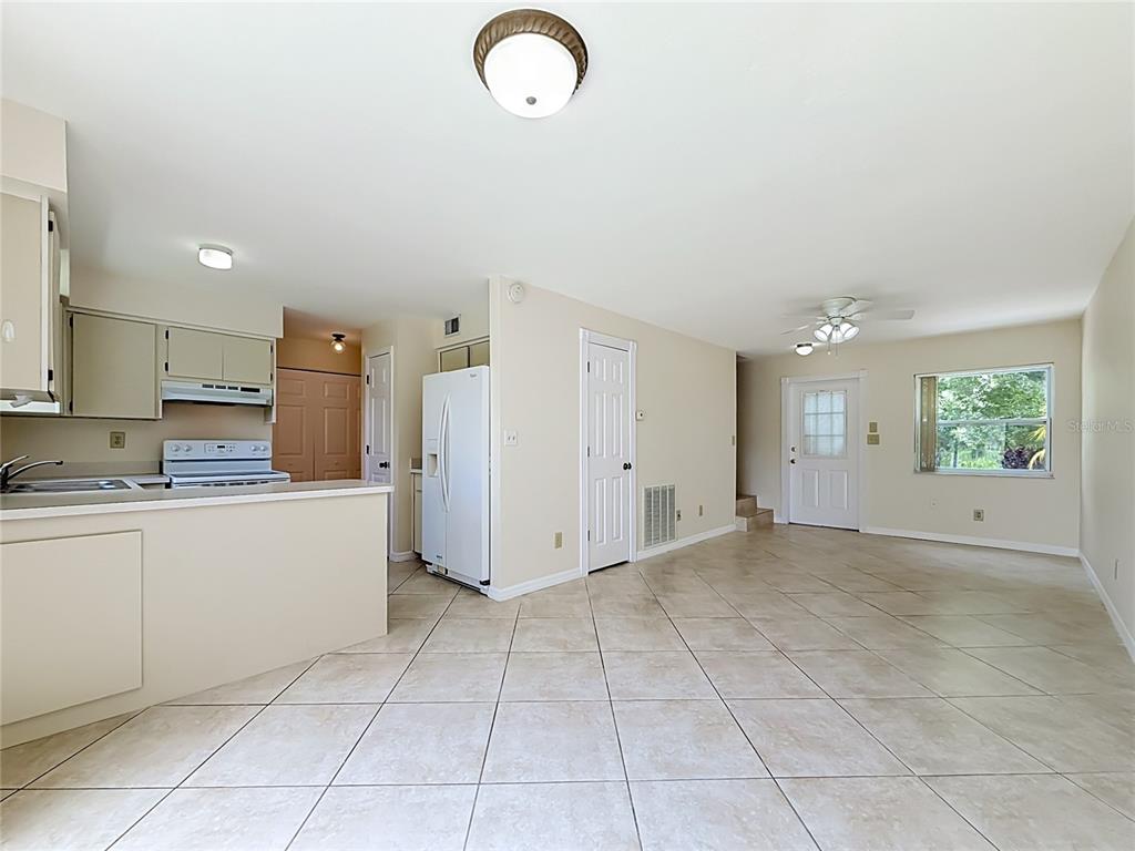 A kitchen with beige cabinets and white appliances opens into a tiled living area — 1718 ADAMS CIRCLE S, LARGO, FL
