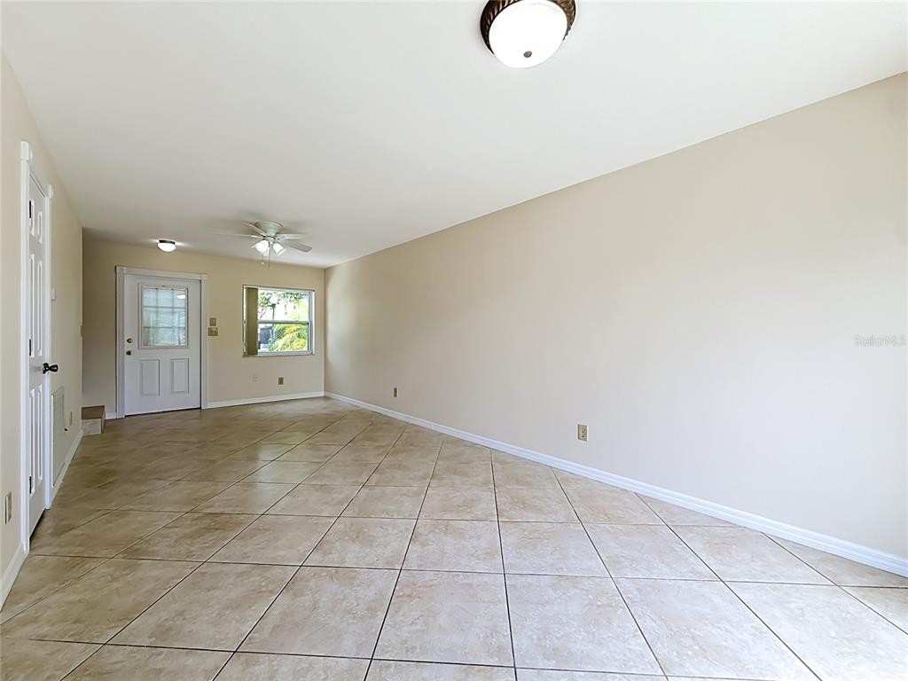 An empty living room features beige walls, a white ceiling, and diagonal tan floor tiles — 1718 ADAMS CIRCLE S, LARGO, FL