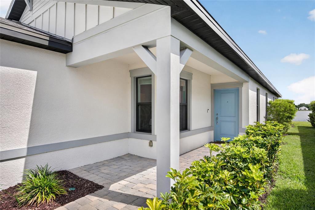 A covered front porch with a blue door, stone pavers, and a white support column — 6492 SILVERSTAR DRIVE, SARASOTA, FL