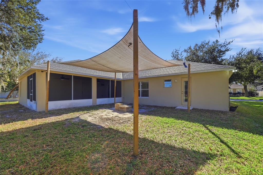 A backyard features a tan shade sail supported by wooden posts over a fire pit — 539 GRANITE CIRCLE, CHULUOTA, FL