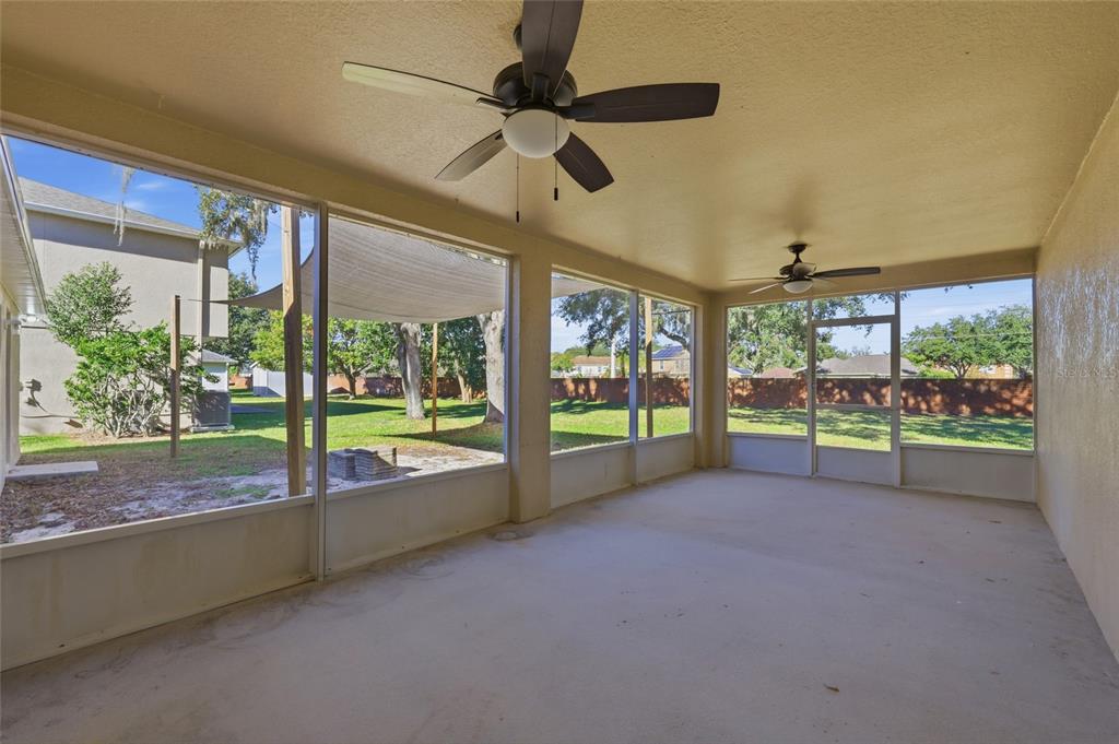 A covered, screened-in patio features two ceiling fans, concrete flooring, and views of a backyard — 539 GRANITE CIRCLE, CHULUOTA, FL