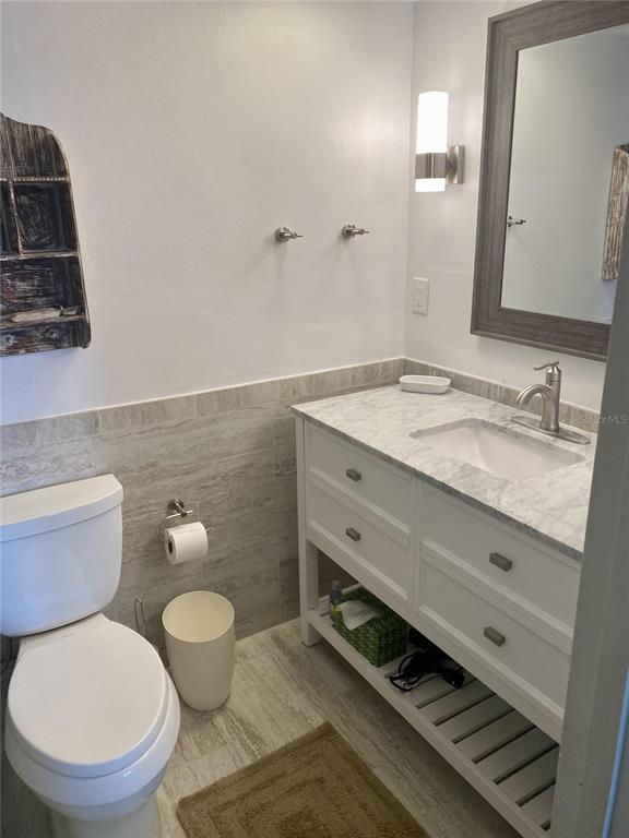 A bathroom features a white vanity with a marble countertop, a toilet, and tiled walls — 815 OCEAN SHORE BOULEVARD UNIT 8A, ORMOND BEACH, FL