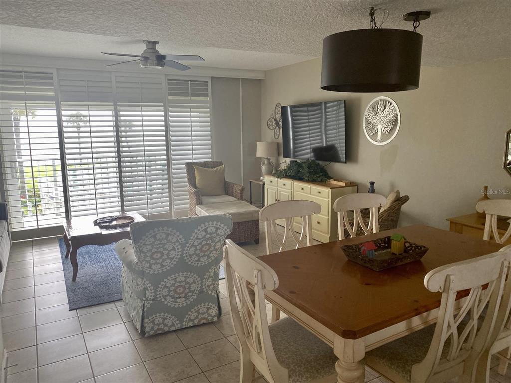 A dining area and living space feature tile floors, a wooden table, and sliding shutters — 815 OCEAN SHORE BOULEVARD UNIT 8A, ORMOND BEACH, FL