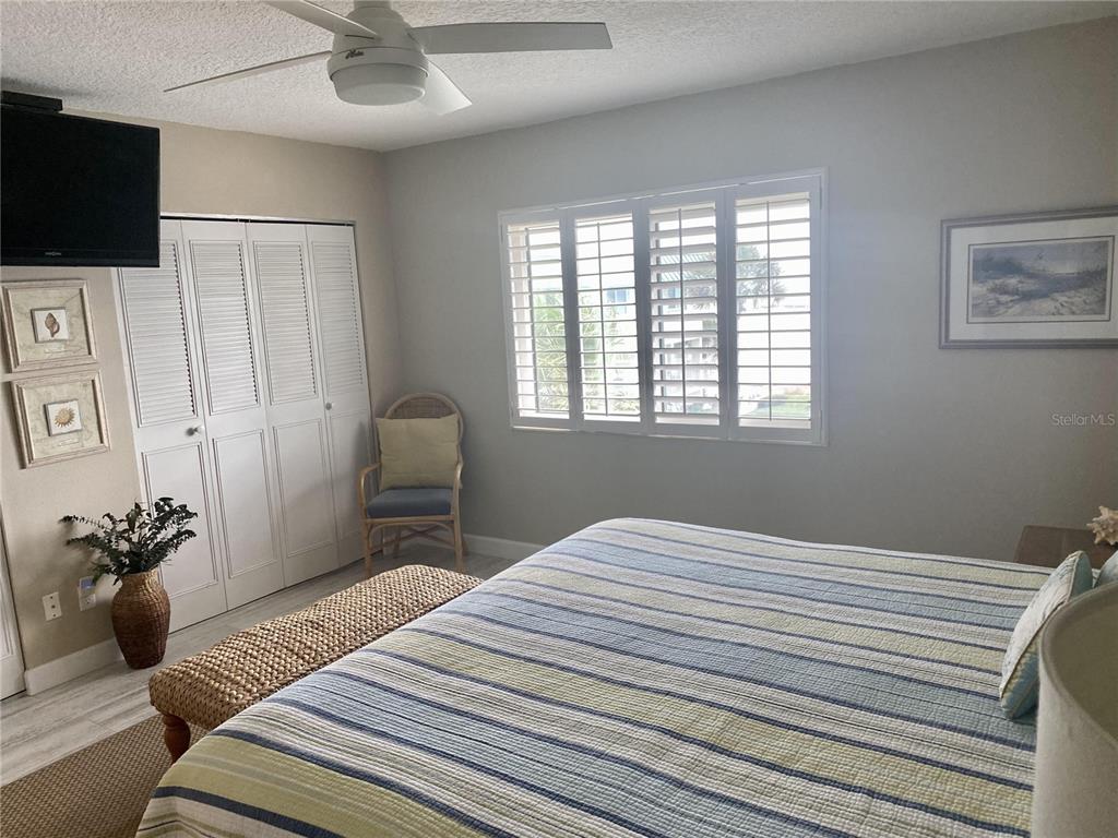 A bedroom features a striped bedspread, a ceiling fan, louvered closet doors, and plantation shutters — 815 OCEAN SHORE BOULEVARD UNIT 8A, ORMOND BEACH, FL