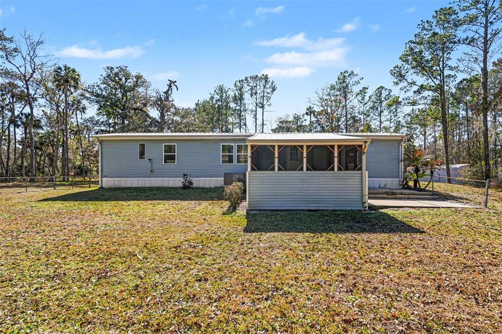 The exterior of a single-story manufactured home features light blue siding and a screened-in porch — 24421 TRESPASS TRAIL, ASTOR, FL