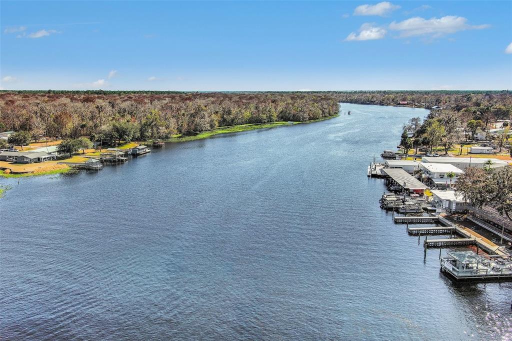 An aerial view shows a wide river lined with docks, boat slips, and forested banks — 24421 TRESPASS TRAIL, ASTOR, FL