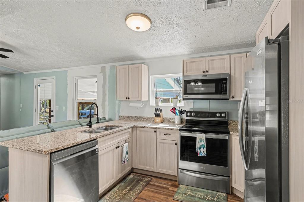 A kitchen features light wood cabinets, granite countertops, stainless steel appliances, and a peninsula sink — 24421 TRESPASS TRAIL, ASTOR, FL