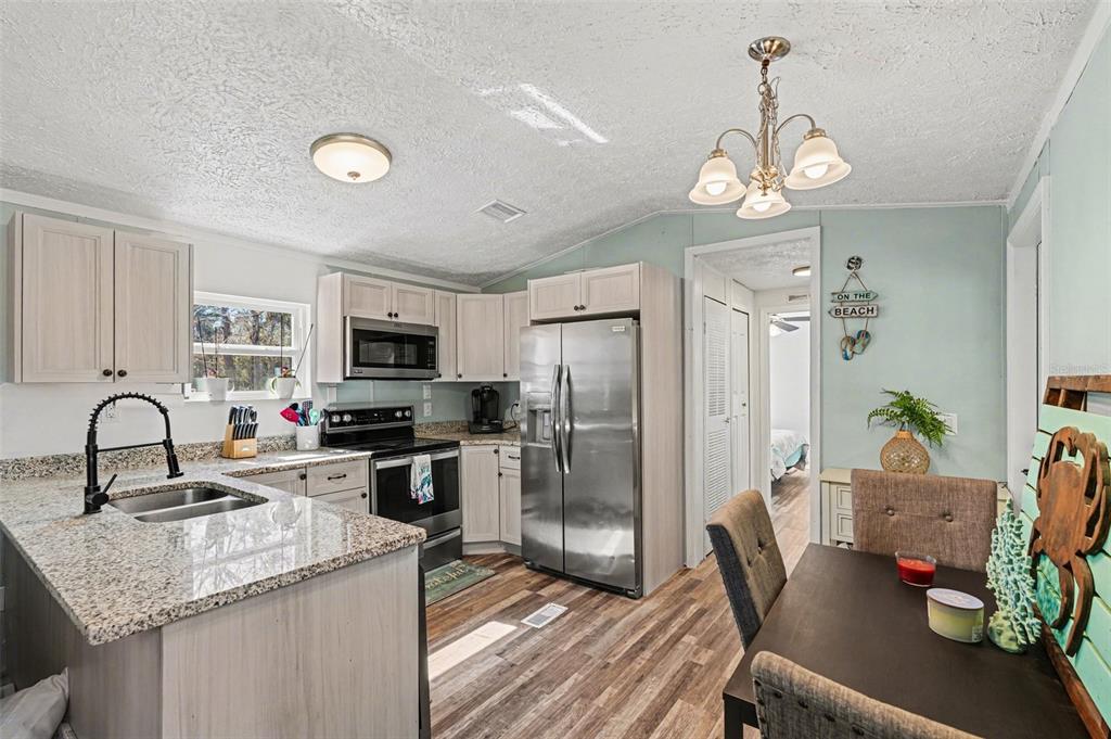 A kitchen with light wood cabinets, granite countertops, stainless steel appliances, and an adjacent dining area — 24421 TRESPASS TRAIL, ASTOR, FL