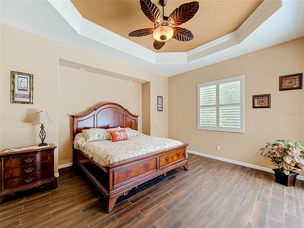 A bedroom features a wooden bed frame, tile flooring, and a tray ceiling with a fan — 27423 NATAL DRIVE, PUNTA GORDA, FL