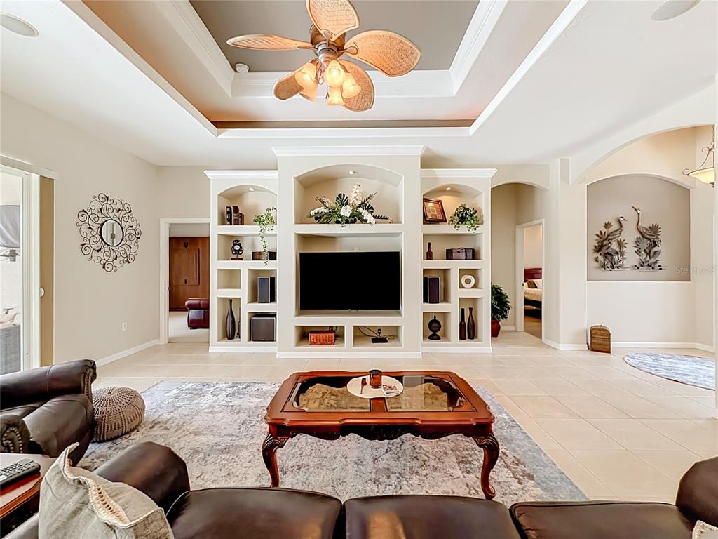 A living room features a large built-in entertainment center, a tray ceiling, and tile flooring — 27423 NATAL DRIVE, PUNTA GORDA, FL