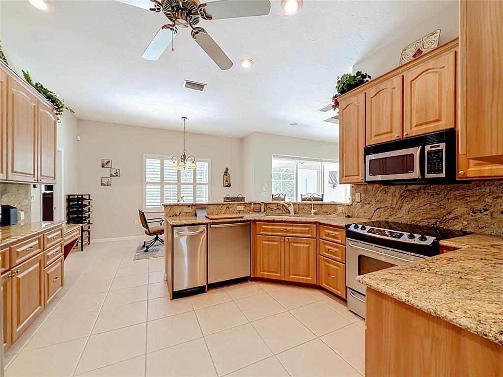 A kitchen with light wood cabinets, granite countertops, stainless steel appliances, and tile flooring — 27423 NATAL DRIVE, PUNTA GORDA, FL