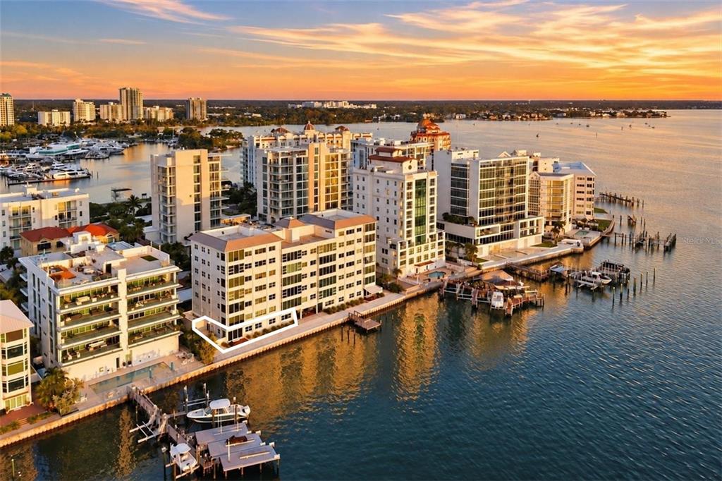 A living room features a fireplace, blue armchairs, a sectional sofa, and floor-to-ceiling waterfront views — 226 GOLDEN GATE POINT UNIT 12, SARASOTA, FL