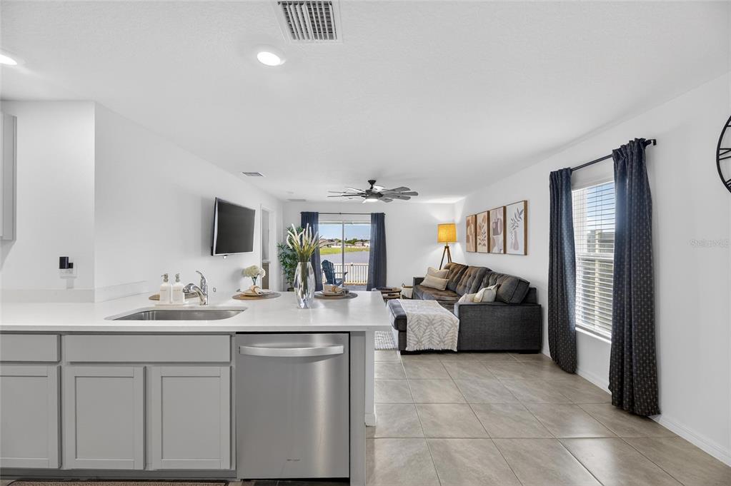 A living room with a gray sectional sofa, a ceiling fan, and an open kitchen — 3345 BLUE ESTUARY ROAD, WIMAUMA, FL