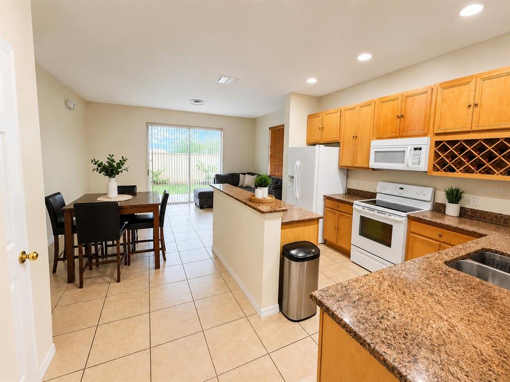 An open-concept kitchen and dining area features tile flooring, granite countertops, and sliding glass doors — 7601 ACKLINS ROAD, KISSIMMEE, FL
