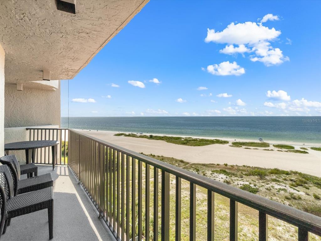 A balcony with outdoor furniture overlooks a sandy beach and the ocean under blue skies — 1290 GULF BOULEVARD UNIT 903, CLEARWATER BEACH, FL