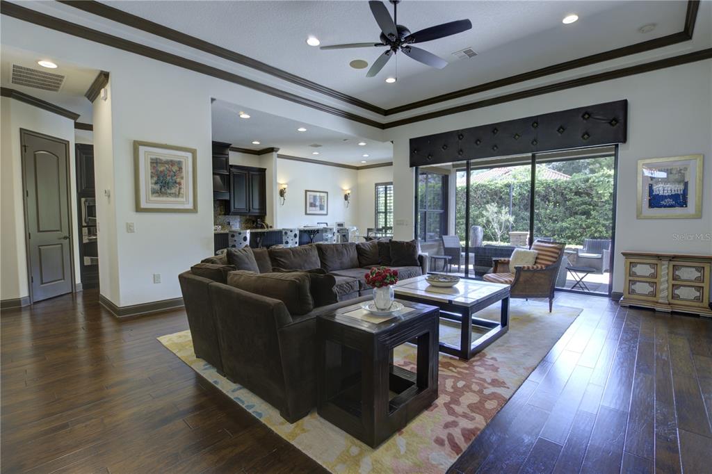 A living room with dark wood floors, a large sectional sofa, and sliding glass doors — 1219 GLENCREST DRIVE, LAKE MARY, FL