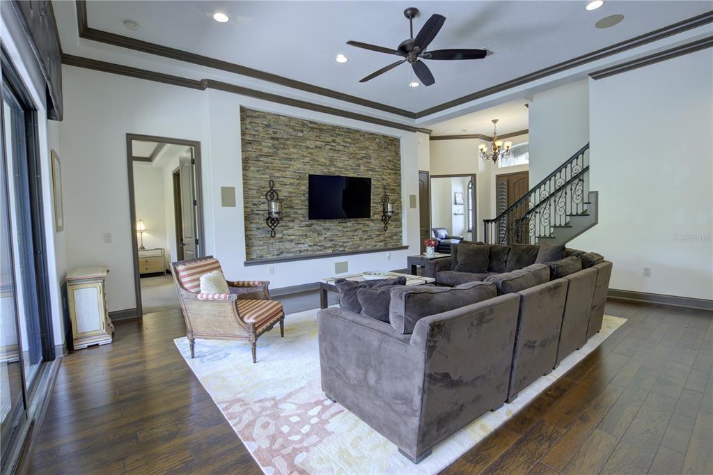 A living room features a stone accent wall with a television, dark wood floors, and furniture — 1219 GLENCREST DRIVE, LAKE MARY, FL
