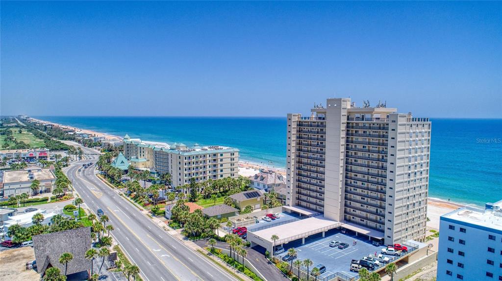 An aerial view shows a tall beachfront condominium building next to a coastal road — 89 S ATLANTIC AVENUE UNIT 204, ORMOND BEACH, FL