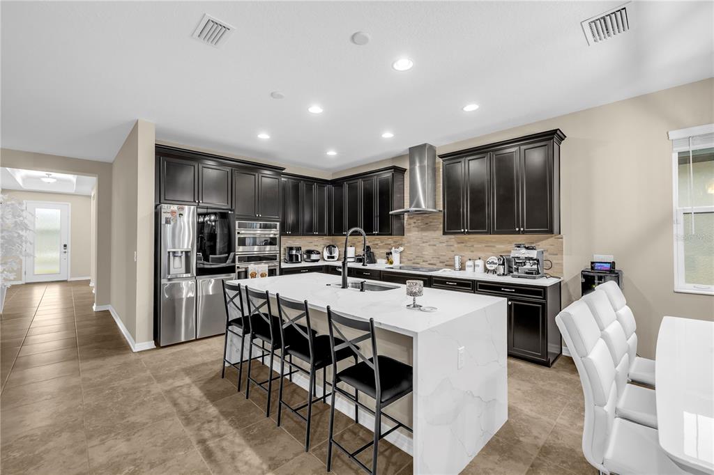 A modern kitchen features dark cabinetry, a white marble island with seating, and stainless appliances — 1937 146TH TERRACE E, PARRISH, FL