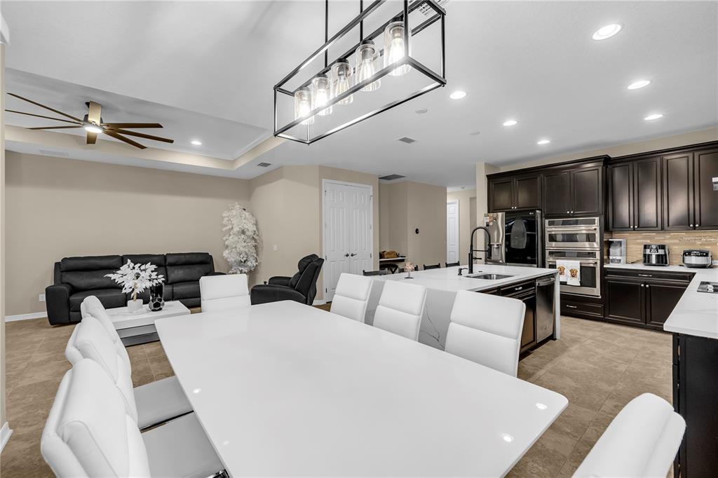 A modern open-concept kitchen and dining area features white tables, white chairs, and dark cabinetry — 1937 146TH TERRACE E, PARRISH, FL