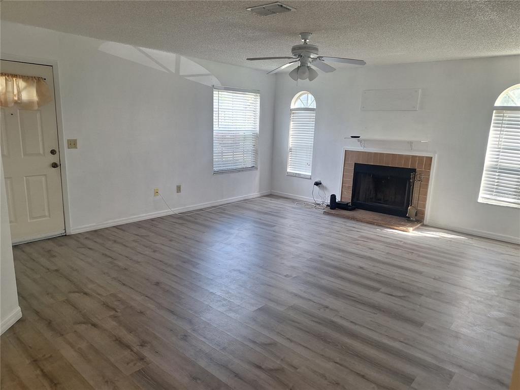 An empty living room features light wood-look flooring, a fireplace, and a ceiling fan — 11910 SKYLAKE PLACE UNIT E, TEMPLE TERRACE, FL