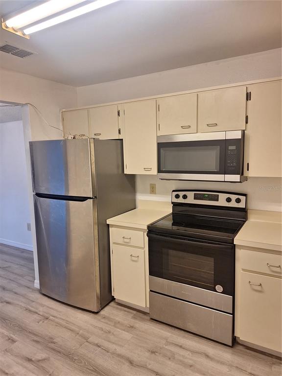 A kitchen features stainless steel appliances, off-white cabinets, and light wood-look flooring — 11910 SKYLAKE PLACE UNIT E, TEMPLE TERRACE, FL