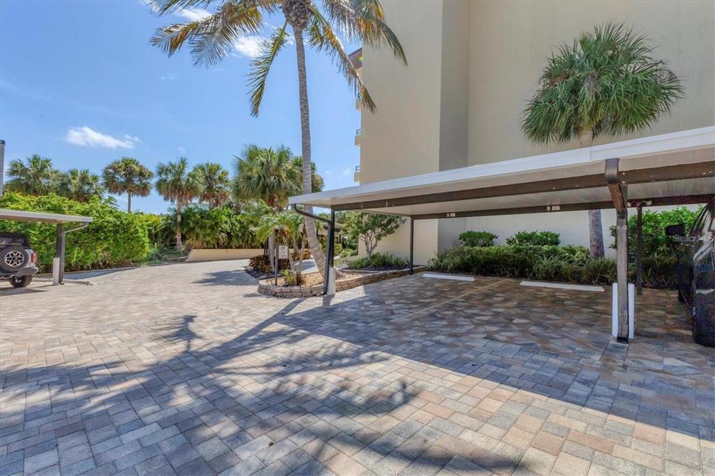 A paved parking area features covered carports next to a building and palm trees — 8776 MIDNIGHT PASS ROAD UNIT C307, SARASOTA, FL