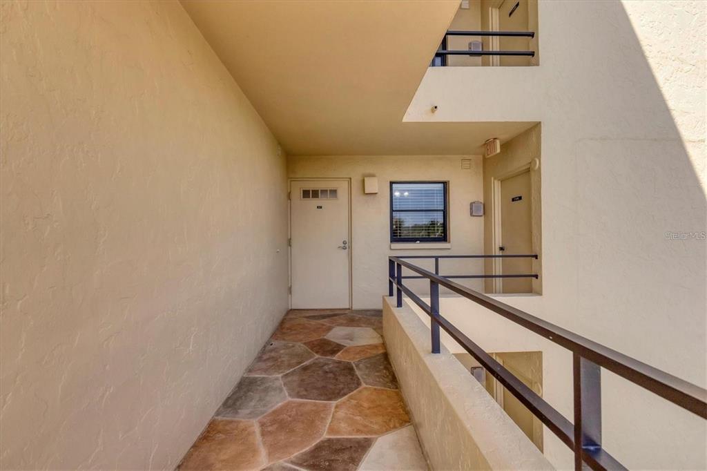 An outdoor walkway with stone-patterned flooring leads to a white door and a window — 8776 MIDNIGHT PASS ROAD UNIT C307, SARASOTA, FL