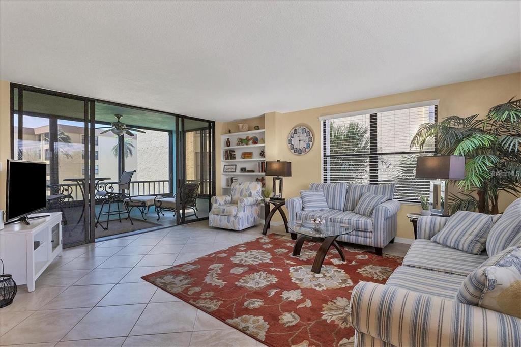 A living room features striped furniture, a large patterned rug, and a sliding door to a balcony — 8776 MIDNIGHT PASS ROAD UNIT C307, SARASOTA, FL