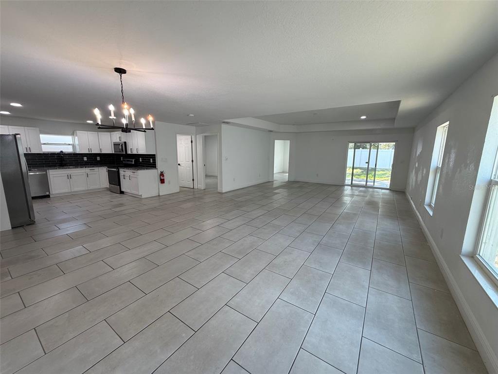 An open-concept kitchen and living area features light gray tile flooring and white cabinetry — 5112 PACIFIC AVENUE, WEEKI WACHEE, FL