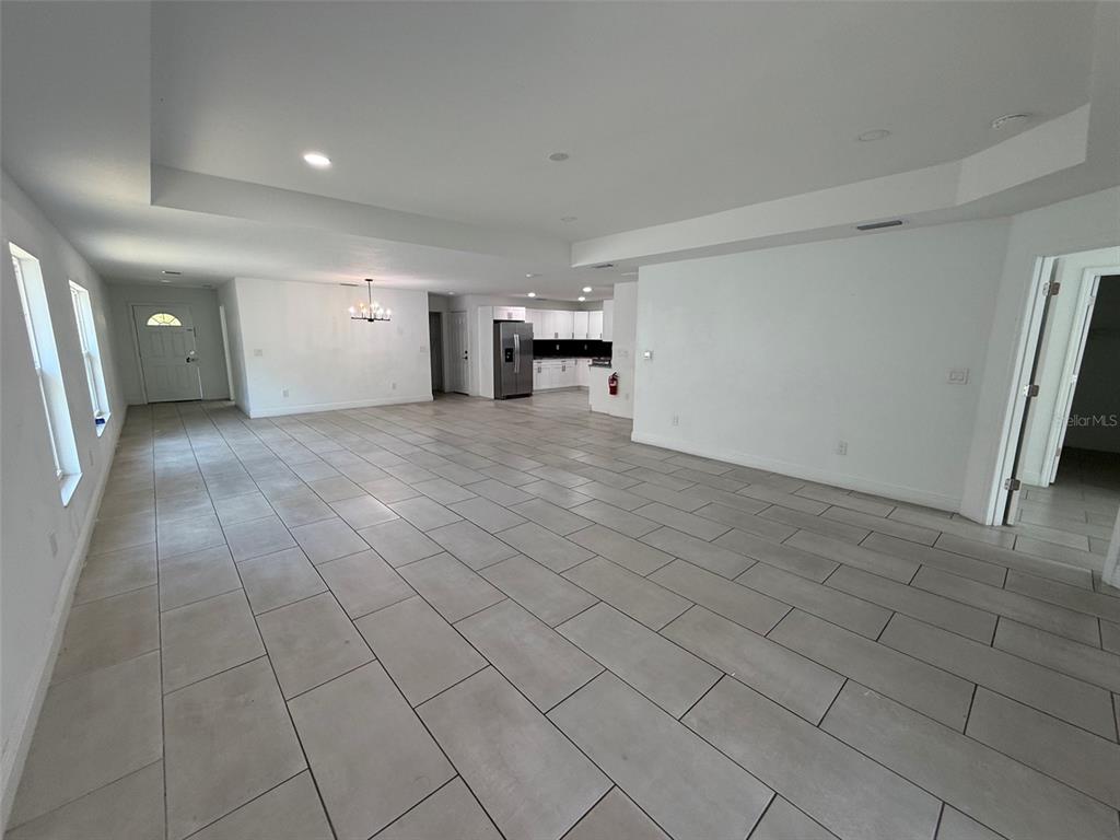 An open-concept living area features large light-colored floor tiles and a kitchen in the background — 5112 PACIFIC AVENUE, WEEKI WACHEE, FL