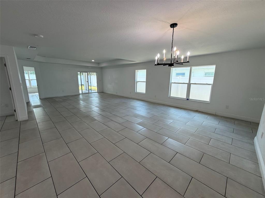 A spacious, unfurnished room features light-colored tile flooring, white walls, and a modern chandelier — 5112 PACIFIC AVENUE, WEEKI WACHEE, FL