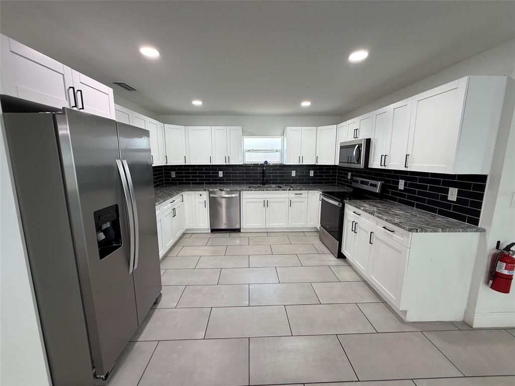 A kitchen features white cabinets, stainless steel appliances, granite countertops, and a black subway tile backsplash — 5112 PACIFIC AVENUE, WEEKI WACHEE, FL